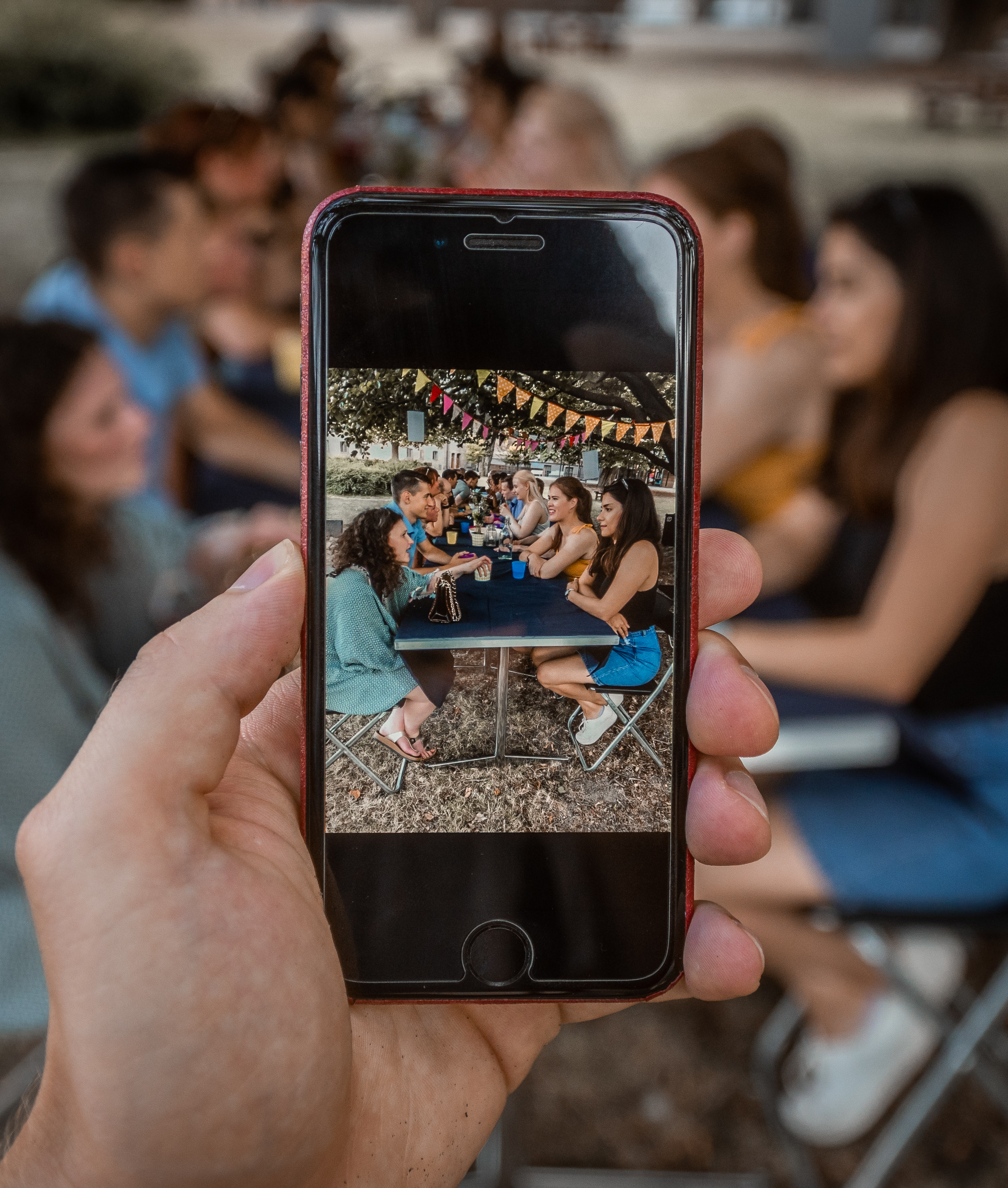 Mobilkamera som tar bilde av en gjeng som sitter i samtaler rundt et langbord på utendørs festival.  
