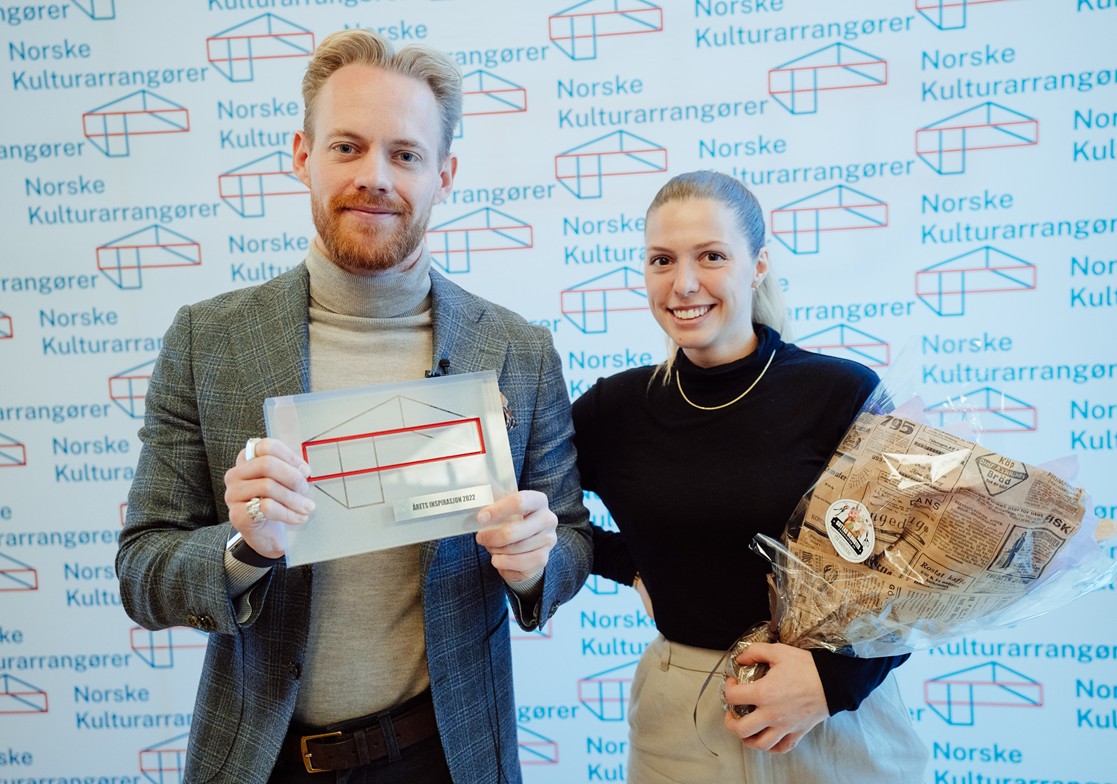 Jørgen Snøås Gustavsen holder prisen som ble tildelt Tons of Rock - Årets inspirasjon 2022. Hans kollega Eirin Martina Bonnevier Berg bærer en blomsterbukett og smiler stolt.