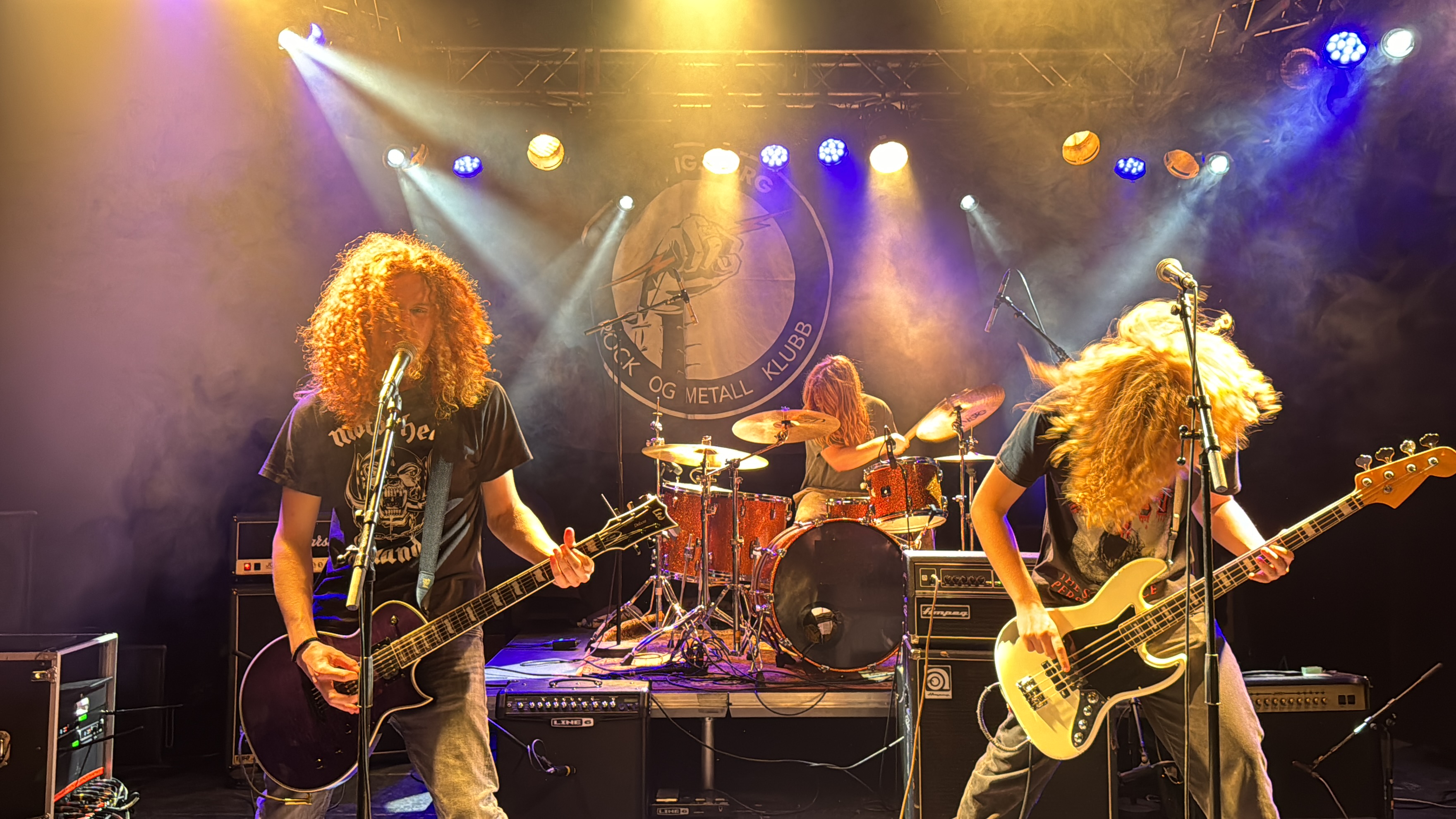 Energisk rockeband spiller på en lyssatt scene. Langhårete gitarist og bassist i forgrunnen, trommis i bakgrunnen. 