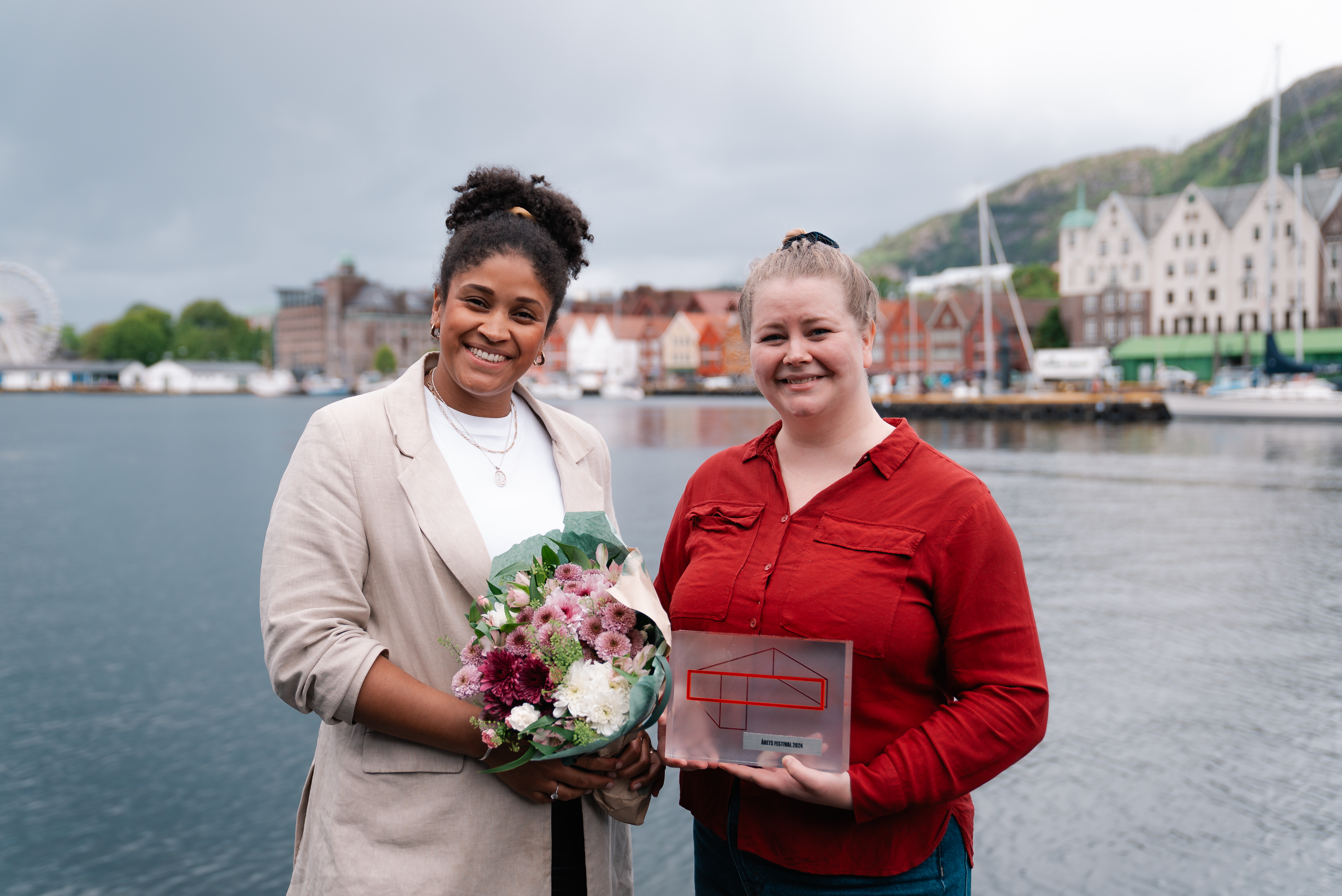 Nyaling og Phoebe smiler bredt til kamera foran Bergen brygge. Phoebe viser stolt frem trofeet for Årets festival 2024.