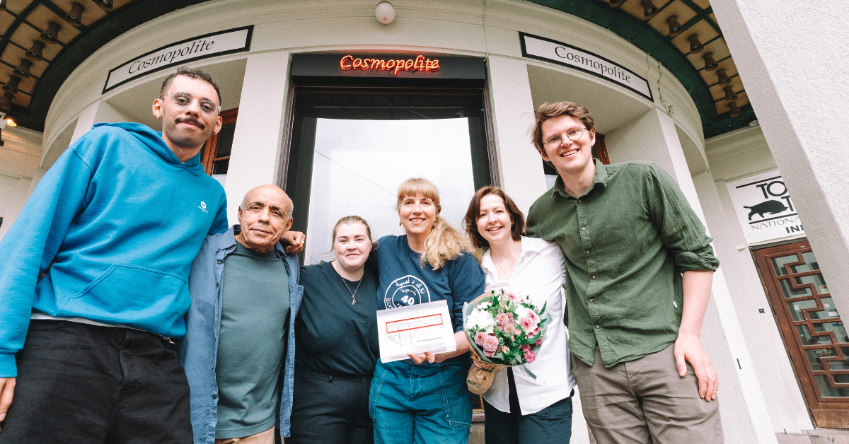 Fire mennesker poserer med en premie og en bukett utenfor et inngangsparti.