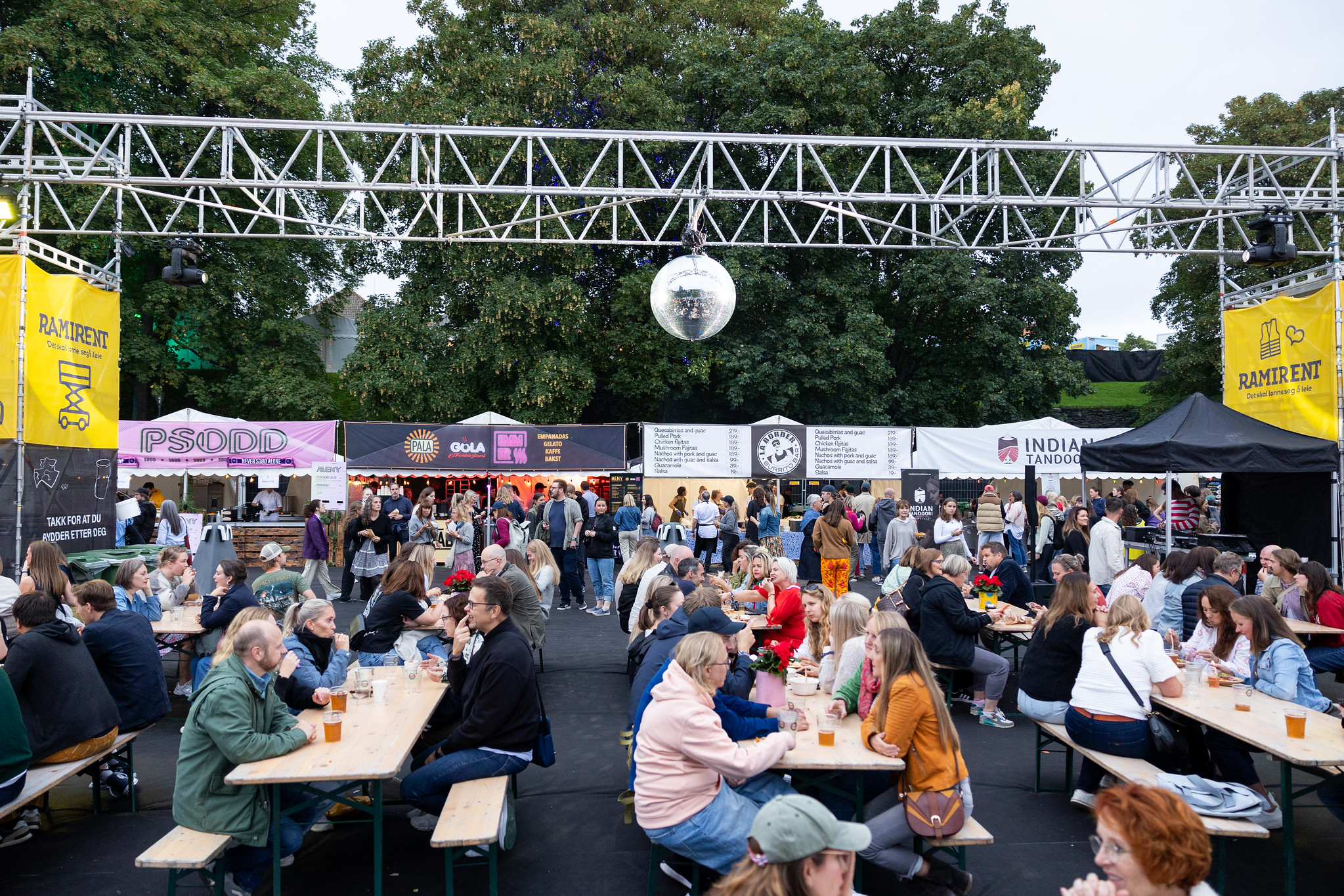 Bildet viser et matområde på en festival med folk som spiser og drikker på langbord.